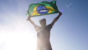 Young man holding brazilian national flag to the sky with two hands at the beach at sunset - Powered by Shutterstock - Get 15% off with code: PIKWIZARD15