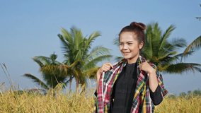 4k video of Asian girl standing and smiling in her rice field in the sun at dawn.