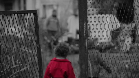 View through lattice gate on gypsy ruined house. Sin city effect, black and white, only red color. Two little kids come home from begging and man preparing firewood. Children in focus, father blurred.