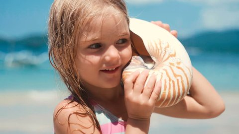 Little girl listen to sea shell on beach