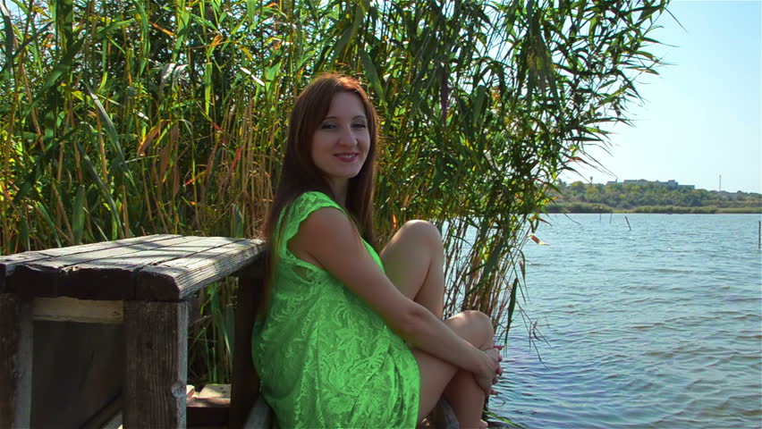 Young woman in green dress smiles and enjoys life on river bank in provincial town