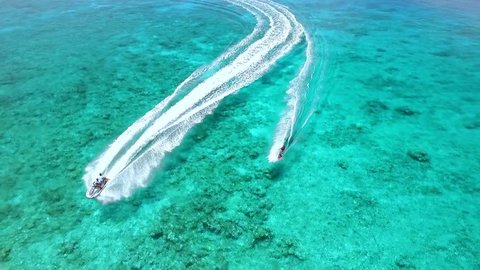 
Jet skiing sport in the blue, crystal clear sea at a coral reef lagoon next to white sand isle. A FHD slow motion drone footage, shot from above.

