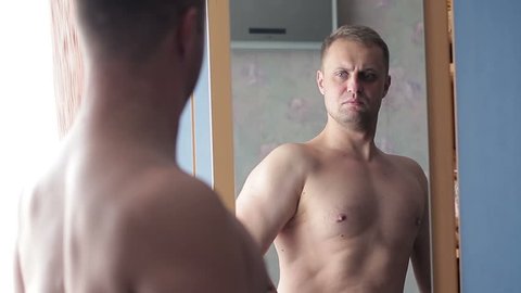 The guy is adorable looking in the mirror. A young man strains his muscles and loves himself