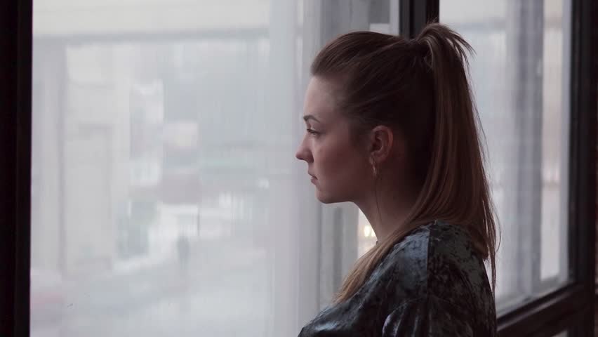 Unhappy young woman looks out the window, bad weather outside | Shutterstock HD Video #1006894570