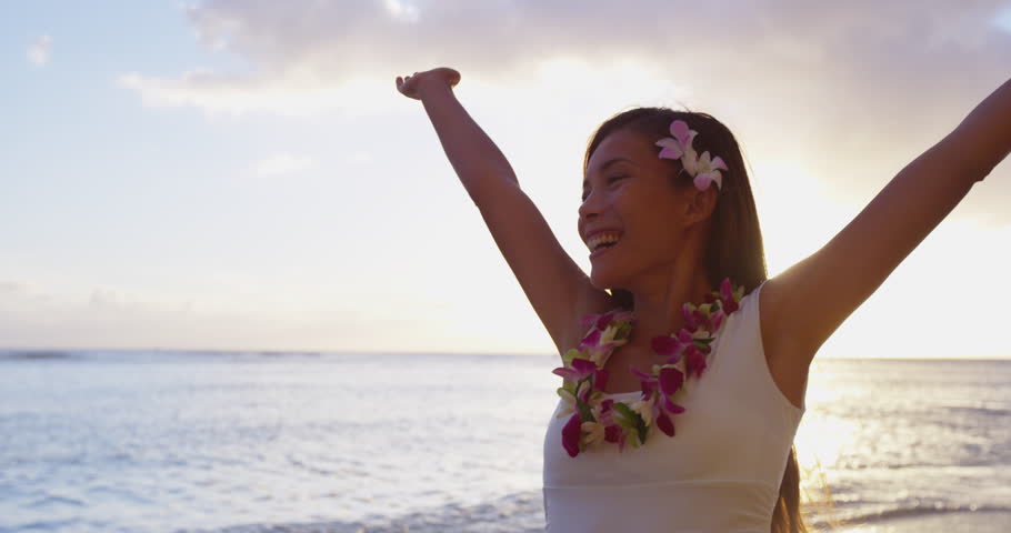 Happy serene woman relaxing on hawaii beach praising freedom smiling on hawaiian beach wearing dress and lei with arms stretched out. Mixed race female model enjoying sun in meditation zen. RED EPIC.