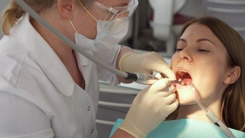 Dentist treating teeth to woman patient in clinic. Female professional doctor stomatologist at work. Dental equipment on background. Dental check up