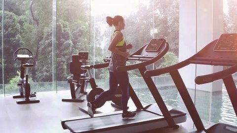 SLOW MOTION. Cute Asian girl on treadmill at gym. Panoramic window, healthy fitness lifestyle concept