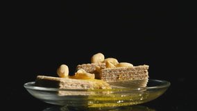 hand takes waffles with honey and nuts in a bowl on a black background
