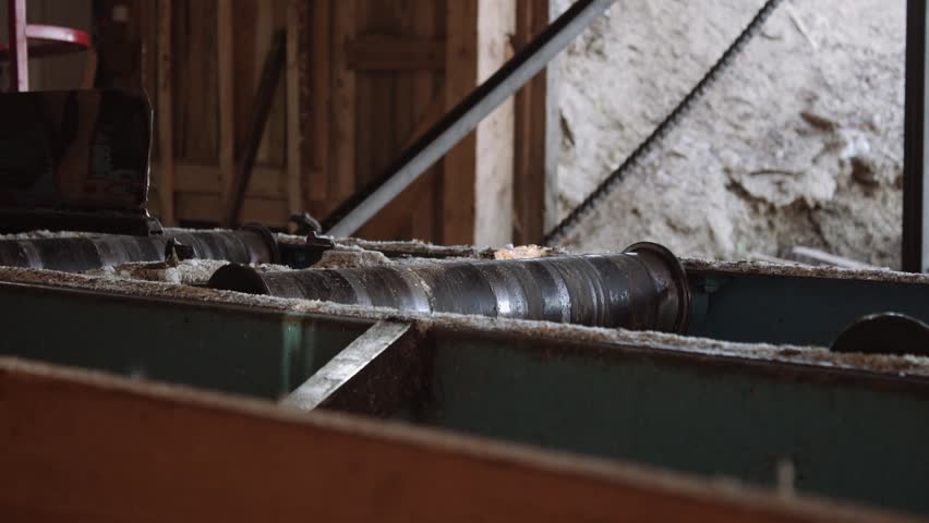 Sawmill machine cutting wood lumber board, rolling metal cylinders, lots of sawdust