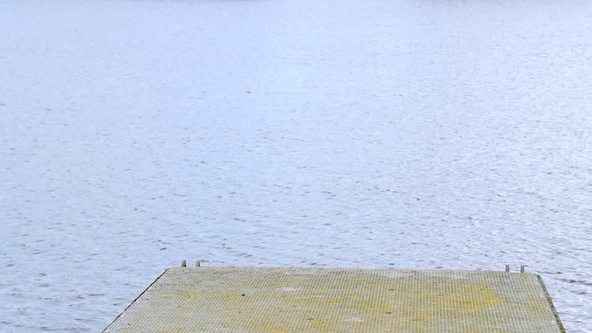 Slow motion - Hipster man walks to the end of pier on a windy cold day with beard and hat on and rolled up jeans and boots
