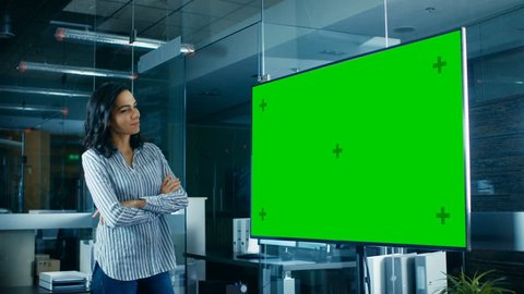 Late at Night Beautiful Hispanic Woman Looks at Mock-up Chroma Key Green Screen TV in the Conference Room. Shot on RED EPIC-W 8K Helium Cinema Camera.