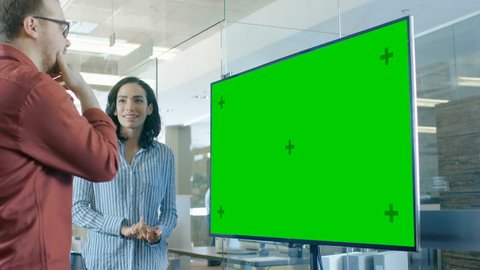 Late at Night Male and Female Business People in Conference Room Have Discussion about Mock-up Chroma Key Green Screen TV. Shot on RED EPIC-W 8K Helium Cinema Camera.