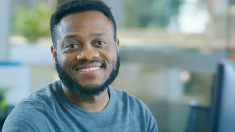 Young Black Man Works on a Personal Computer Charmingly Smiles on Camera. Stylish Smart Man with a Trimmed Beard. Shot on RED EPIC-W 8K Helium Cinema Camera.
