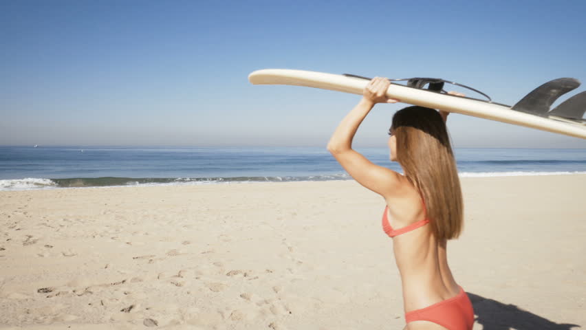 young woman carrying a surfboard at the beach in california.