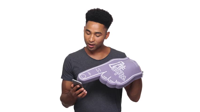 Smiling african man in t-shirt using smartphone and wearing foam finger over white background