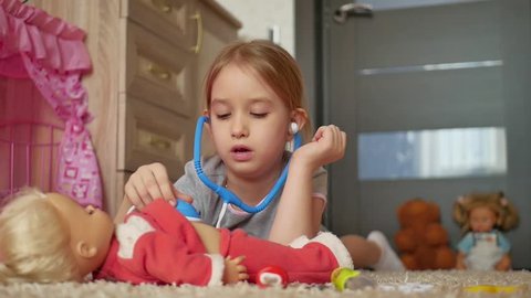 Beautiful little girl playing doctors with doll at home.