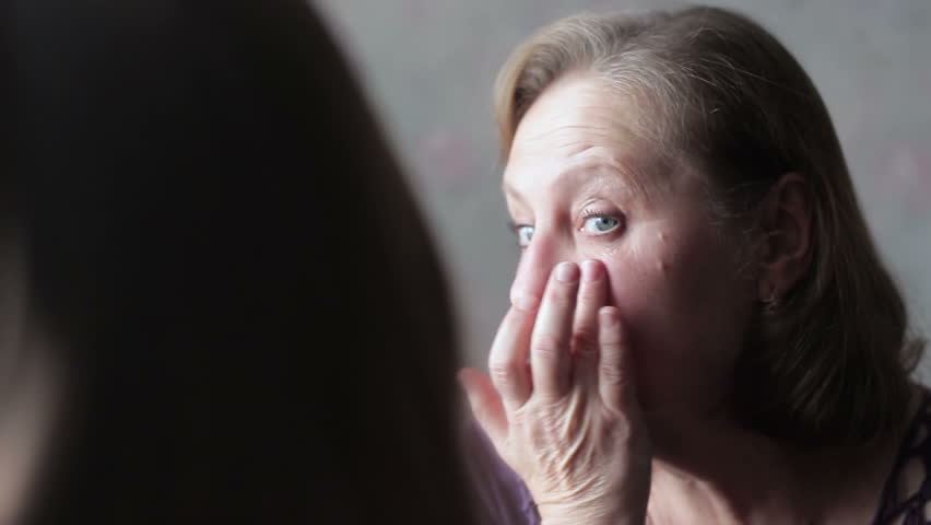 Elderly woman staring at herself in the mirror. Bruises and bags under the eyes, the aging skin of an elderly woman Royalty-Free Stock Footage #1006930903