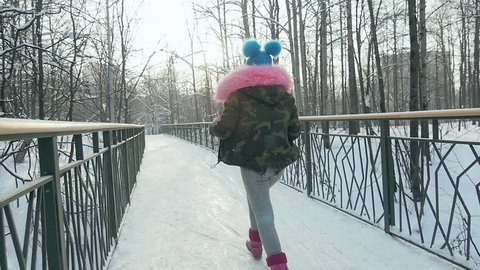 A girl Runs across a Bridge and having Fun. Winter clothes military blue hat
