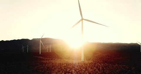 Windmill spinning at sunset in desert with lens flare creating clean energy