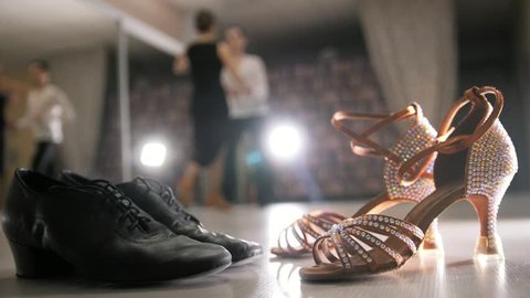 Blurred professional man and woman dancing Latin dance in costumes in studio, two pairs ballroom shoes in the foreground