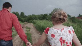 Cute couple under the rain in the park. Clip. A pair of runs in the rain holding hands in the countryside