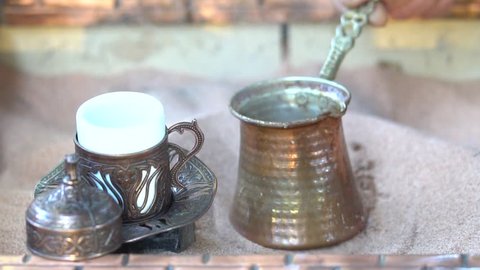 Making turkish coffee in copper cezve over hot sand. Milling of grains. On the hot sand Turk with a running coffee. Running coffee close up. hot sand with burning fire. A cup of coffee.