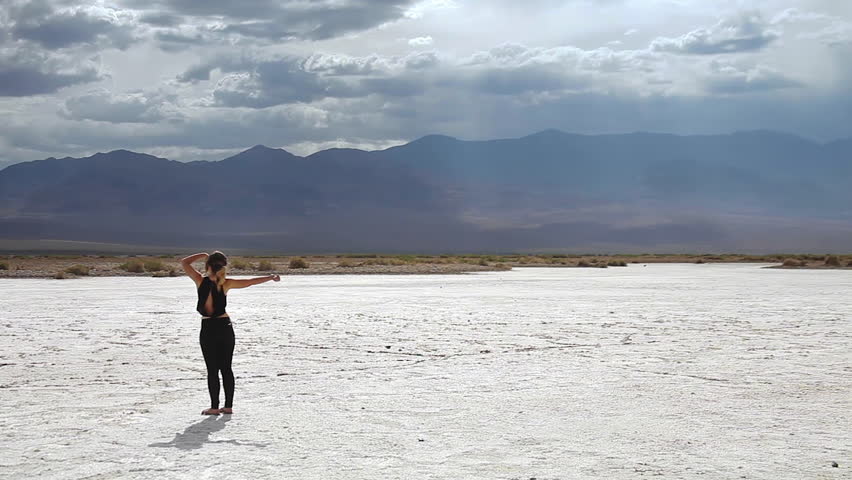 Traveling girl stretching arms in Badwater Death Valley, standing on a salt ground