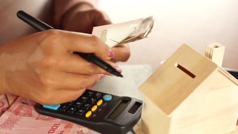 business woman hand counting money paper currency with saving account book ,house model and calculator on desk, planing to buy or rent home