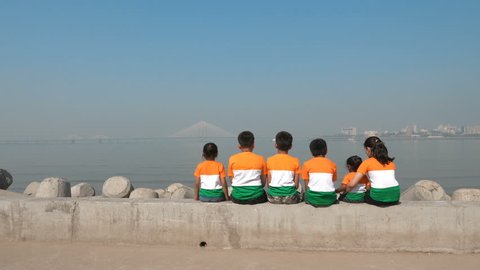 A group of children wearing Indian flag tricolor t-shirts sitting on a platform against Bandra worli sealink built over Arabian sea, Mumbai, India