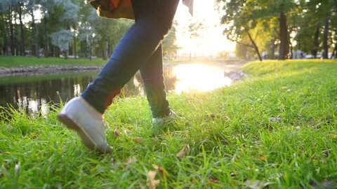 Time out pleasure, elegant woman walk at quiet park on grass at pond bank, low camera, slow motion glide shot. Small silver shoes step on autumn lawn, wonderful evening sun light ahead