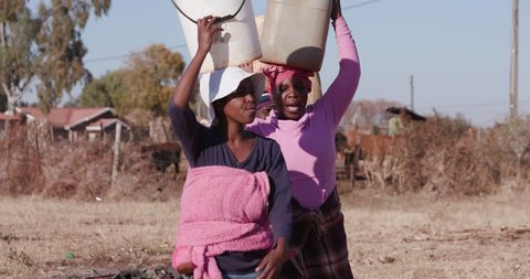 Poor people in Africa unable to maintain social distancing due to water crisis. The plight for fresh water.Three african woman carrying water on their heads in plastic buckets.