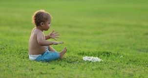 Child getting up from lawn grass green field. Infant toddler baby getting up and walking in green field during sunset golden hour time - 4k clip resolution