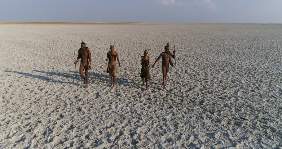 Close-up, then high zoom out aerial view of four Bushman walking across the vast expanse of the Makgadikgadi Pans, Botswana Royalty-Free Stock Footage #1006985140