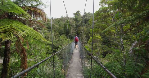 New Zealand tramping hiking man on nature hike in Abel Tasman National Park. Young traveller backpacking crossing suspension bridge over Falls River. RED EPIC in SLOW MOTION.