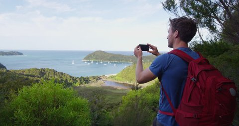 New Zealand travel man taking pictures with smart phone of the Anchorage in Abel Tasman National park, New Zealand vacation. Male backpacker tramping hiking on Abel Tasman Coast Track. SLOW MOTION.