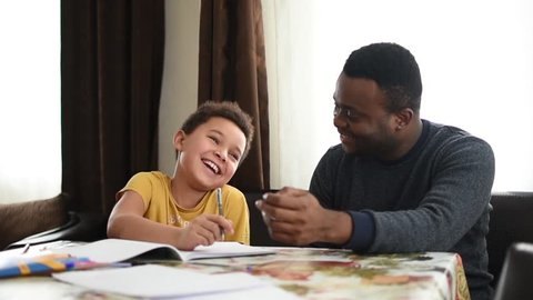 Mixed family at home. African father and african american child. dad helping son with school homework. Education and relationship, man teaching and boy learning. home schooling.
