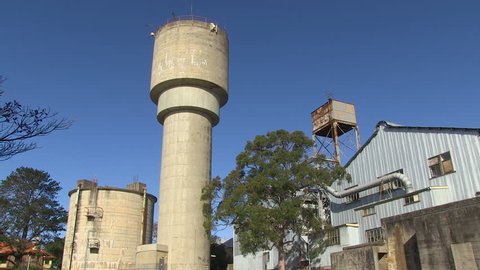 A wide shot of a tower and a warehouse with trees. Camera pans to the left