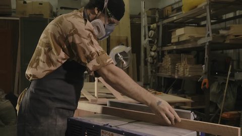 profession, people, carpentry, woodwork and people concept - carpenter working with plane and wood plank at workshop