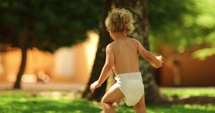 Candid beautiful shot of infant toddler with diapers outside in the sunlight in 4k clip resolution. Toddler kid in diapers holding a pear fruit outdoors