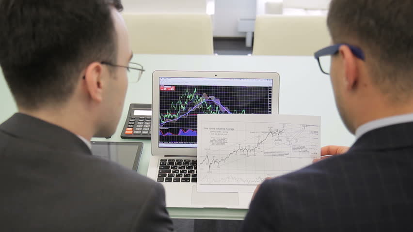 The two finance analytics work on the final report using the brand new laptop and draft. The colleagues look at the charts on the screen and compare the data with information on the paper. Men wears | Shutterstock HD Video #1007004772