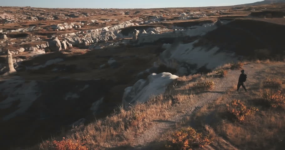 High angle aerial view orbiting man walking in on high ridge above fairy chimney landscape and Goreme town in Cappadocia, Turkey. 4k at 23.97fps