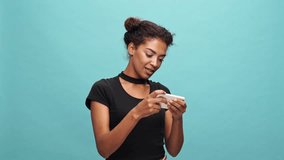 Happy african woman in t-shirt playing smartphone over blue background
