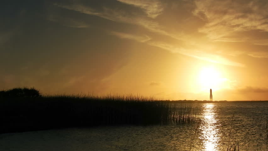 4k Futuristic or Sci-fi landscape.  Low setting sun with wonderful reflection and large rocket ship blasting off with enormous plume of smoke.