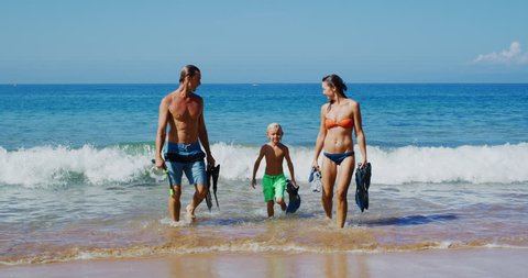 Young family walking out of the ocean with snorkel gear on vacation