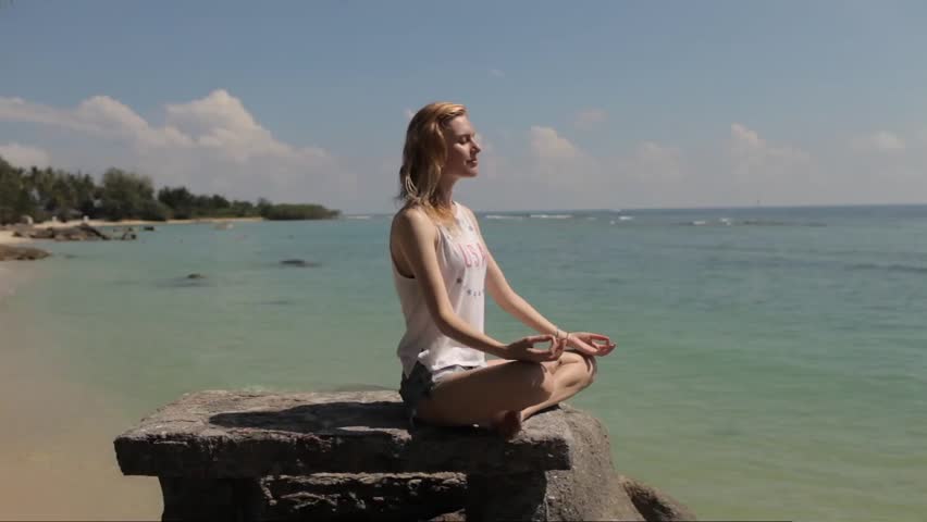 woman meditating on a stone on a tropical beach