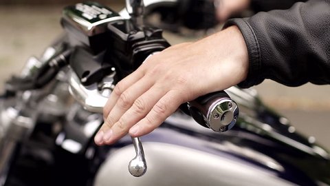 Close-up of a man squeezes the clutch on the handlebars of a motorcycle. Close-up of man's hand on handlebars of motorcycle.