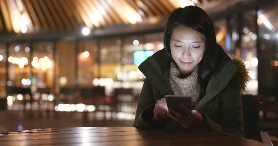 Woman using smart phone outside restaurant at night