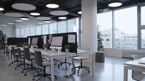Tracking shot of empty open space office with stylish interior, panoramic window, comfortable furniture and modern computers