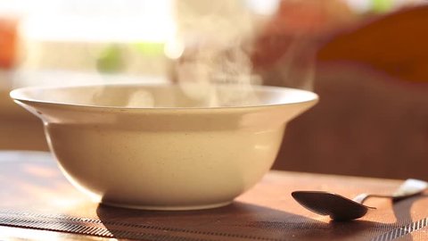hot soup in a plate, steam rises above a white ceramic plate, next to it lies a spoon