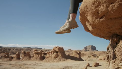 Legs of woman sitting on the edge of rock formation in desert / Goblin Valley, Utah, United States